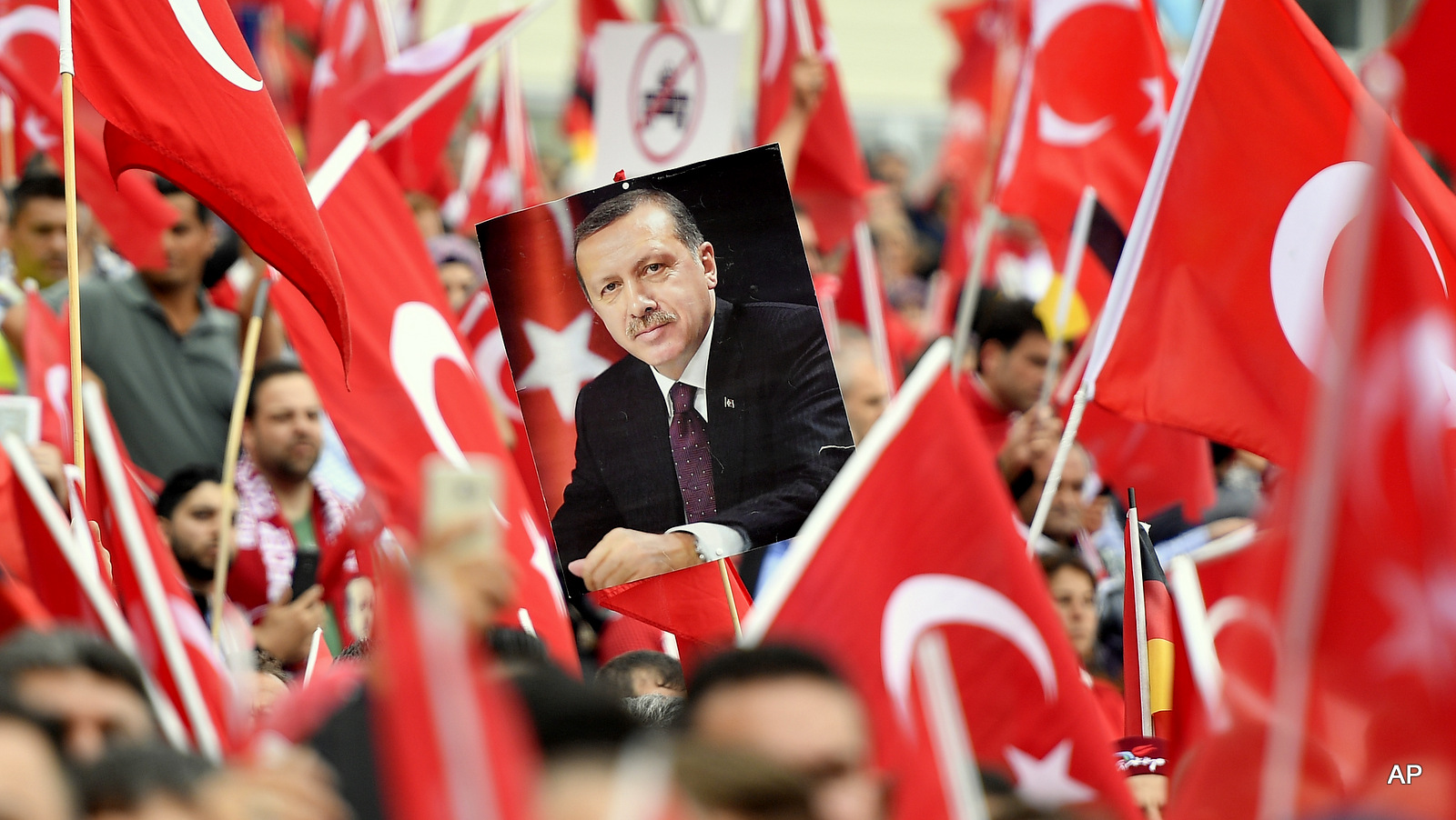 A picture of Turkish president Erdogan is framed by national flags during a demonstration in Cologne, Germany, Sunday, July 31, 2016. Thousands of supporters of Turkish President Recep Tayyip Erdogan have gathered in the German city of Cologne for a demonstration against the failed July 15 coup in Turkey. (AP Photo/Martin Meissner)